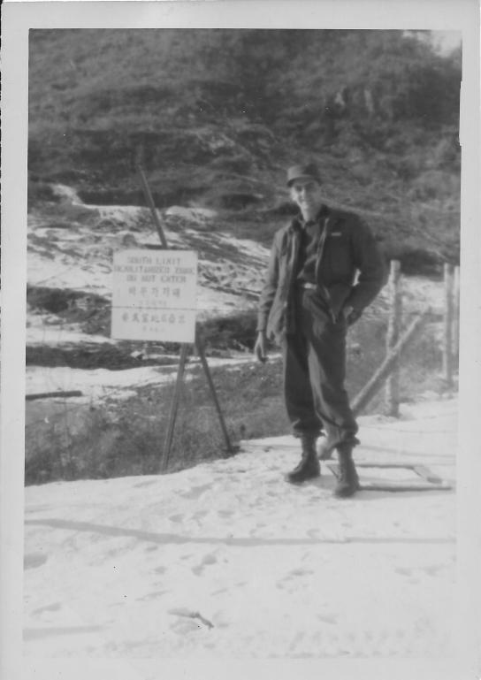 Caption: refer pix #2 Jan 1, 1954 New Years Day. On the way back from the 25th Inf. Div. QM we went offcourse to take this pix. My first look at the DZ (Demilitarized) - No Man's Land-e Commies on the other side. That's snow on the ground and me, Natch! Sign hung on barbed wire reads "South Limit Demil Zone Do Not Enter" & Korean writing. Armond Small